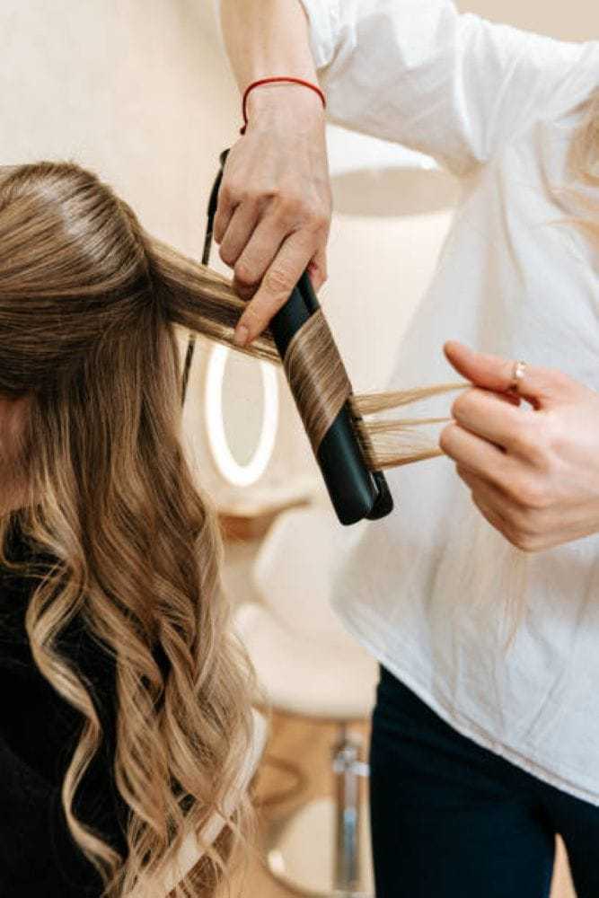 Hairdresser curling client's long hair with a straightener in a salon.