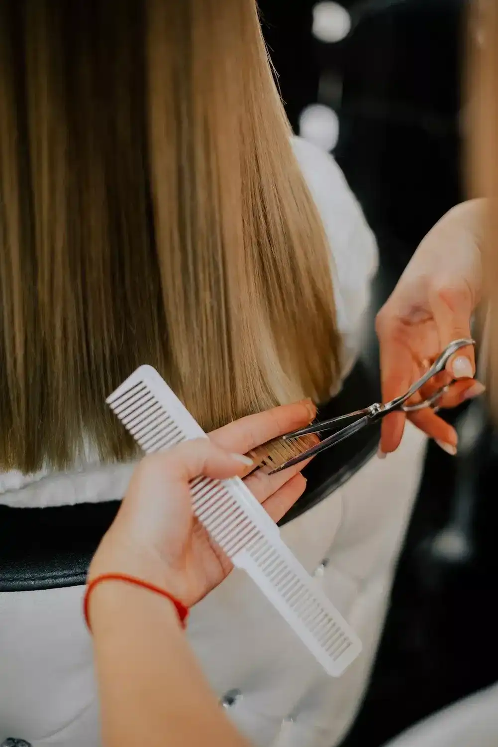 Hairdresser cutting long brown hair with scissors and comb indoors.